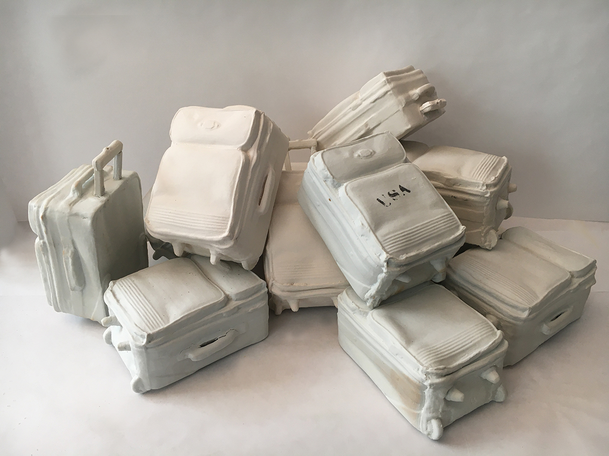 Joy Nagy porcelain clay sculptures of miniature suitcases arrayed to suggest the plight of today's immigrant. 