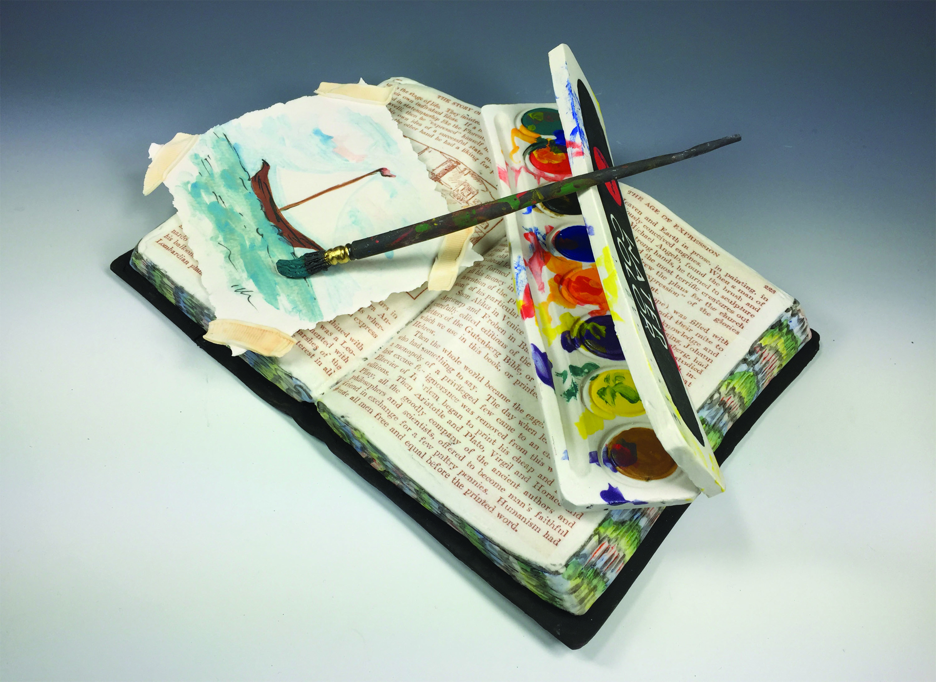 Suzanne Sidebottom used porcelain clay, underglazes and ceramic decals to create a realistic image of an open book, a palette and a paint brush on top of a small painting with tape on the corners.